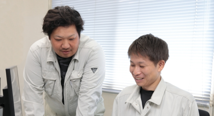 オフィスで話し合う作業着の男性二人。