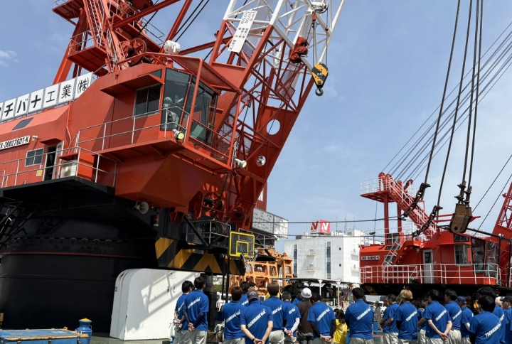 大型クレーンの前で作業員が集まっている工事現場の様子。