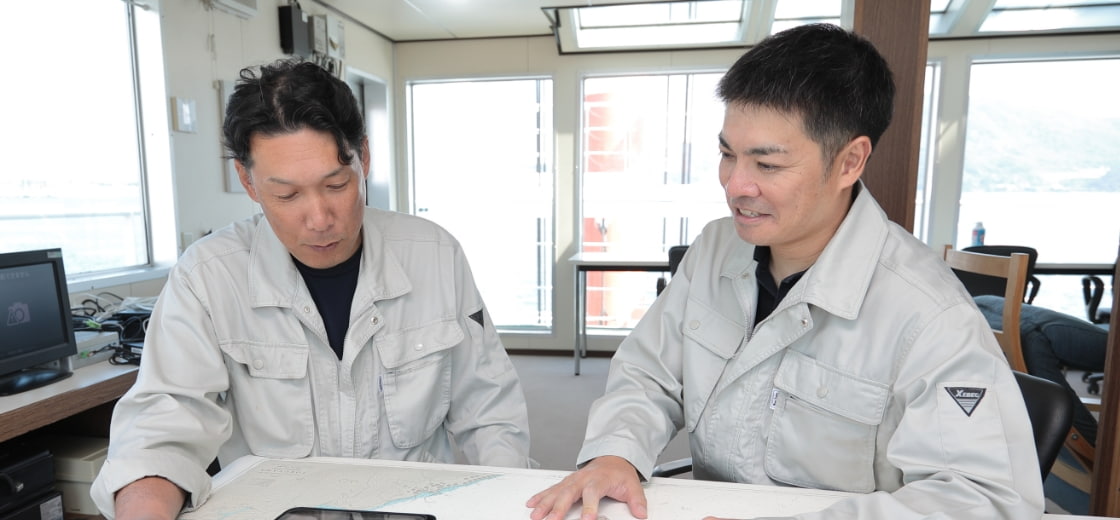 工事計画を話し合う作業服を着た二人の男性スタッフ