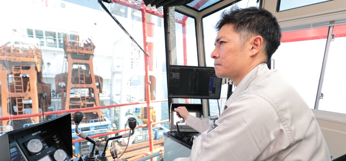 クレーン操作室で機械を操作する作業員、港湾作業の安全管理風景。