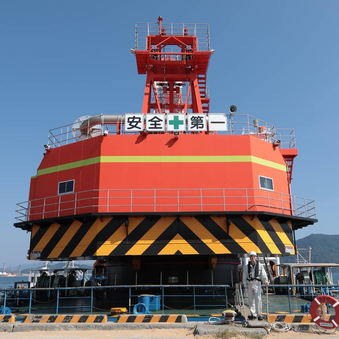 港に停泊している赤と黒の海洋構造物と作業員の画像