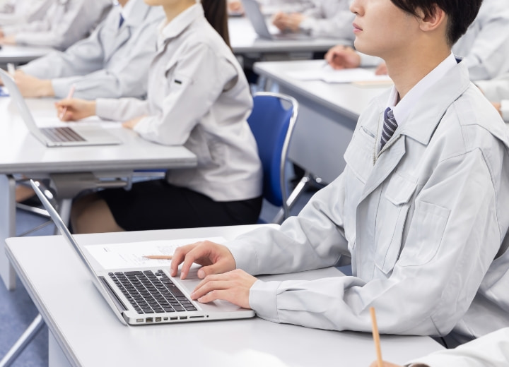 工場の制服を着た学生がパソコンで研修を受けている教室の様子