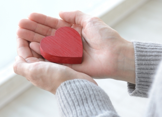 手のひらに赤い木製のハートを持つ女性の手のクローズアップ。