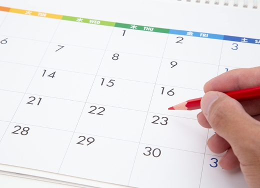 手帳のカレンダーに赤い鉛筆で日付を指している画像。