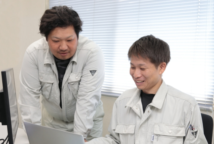 オフィスでパソコン作業をする作業服の二人の男性社員