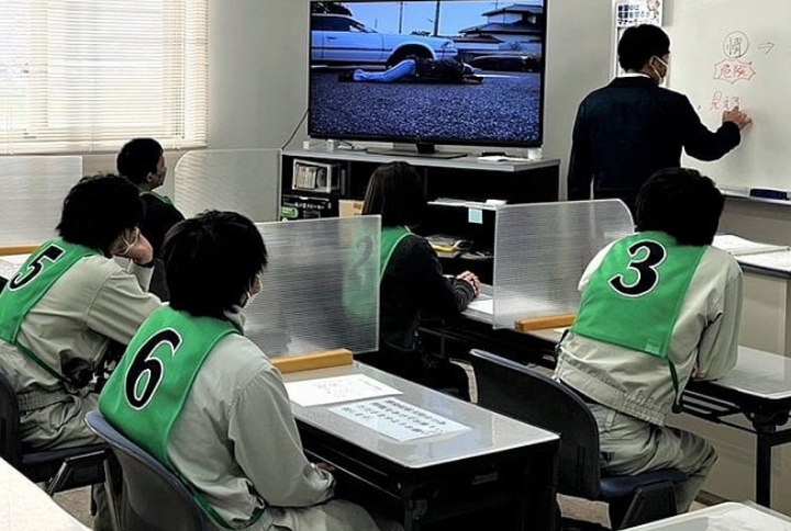 教室で交通安全のビデオを視聴し、講師の説明を聞く研修生たち。
