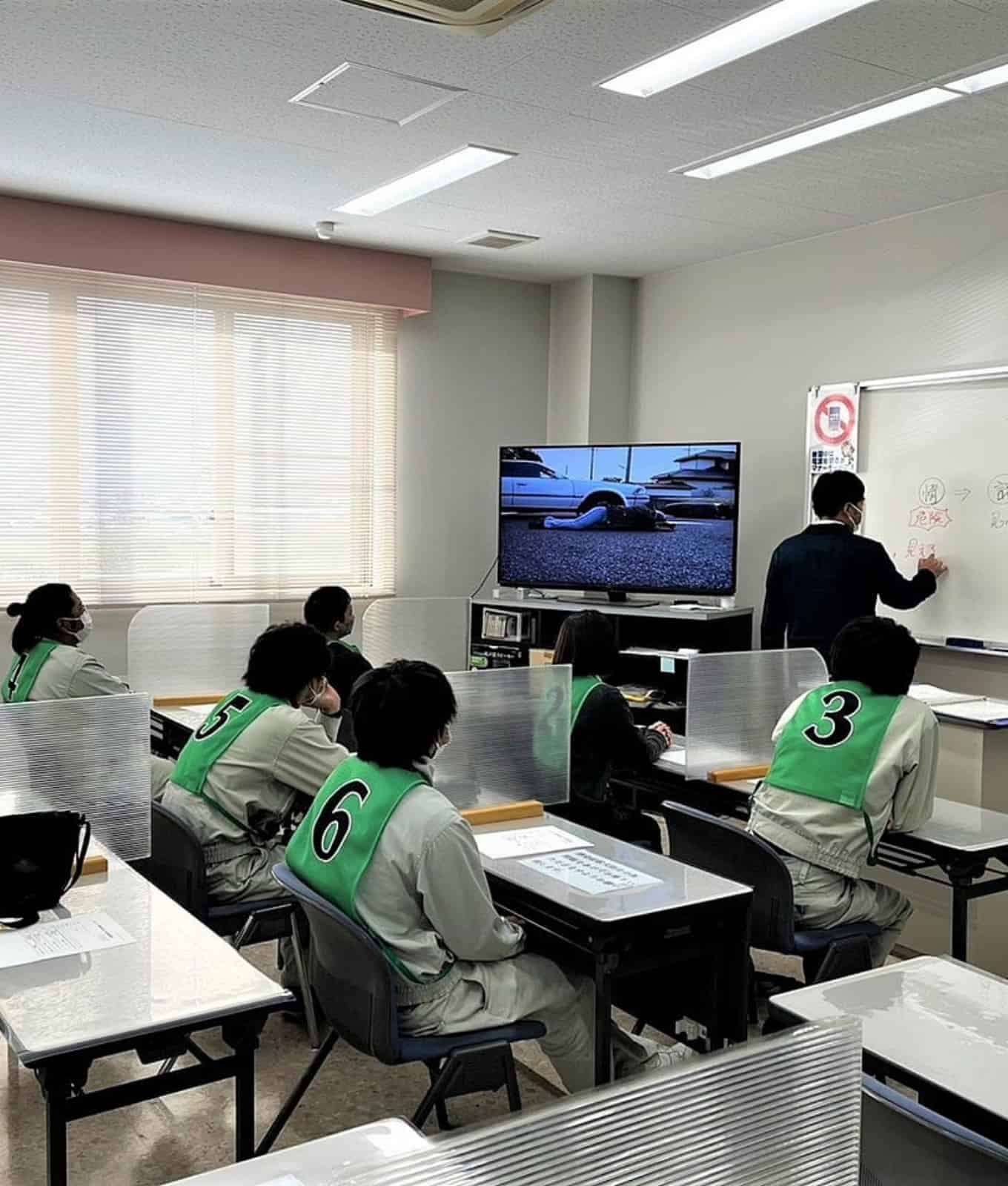 教室で生徒が机に座り、教師が前に立っている様子です。