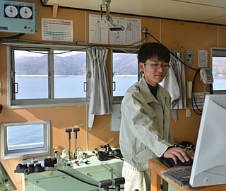 白いシャツを着た眼鏡の男性がコンピュータで作業している様子です。